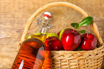 Glass bottle of fresh apple cider vinegar and basket with fruits on wooden background
