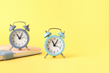 Alarm clocks and notebook on yellow background