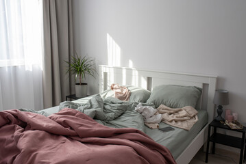 Cluttered bedroom with a pink and mint bedding with clothes thrown on the bed