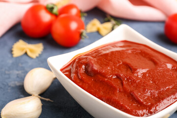 Bowl of tasty tomato paste, garlic cloves and raw farfalle pasta on grey grunge background