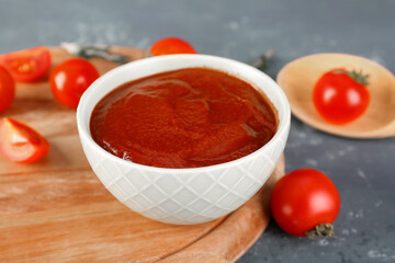 Board with bowl of tasty tomato paste on blue grunge background