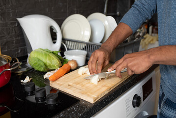 Hands of a young black man cooking at home - chopping onions in the kitchen