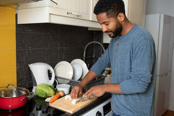 Smiling young black man cooking at home - chopping onions in the kitchen