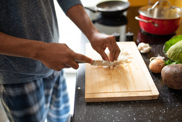Fototapeta na wymiar Hands of a young black man cooking at home - chopping onions in the kitchen