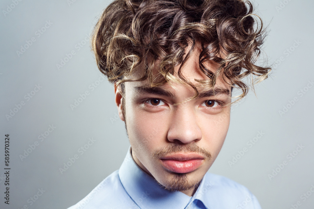 Wall mural handsome man with curly hairstyle, wearing blue shirt, looking at camera with serious expression.