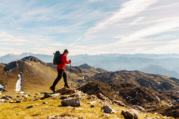 mountaineer man from behind with red clothes, backpack and trekking poles practicing high mountain...