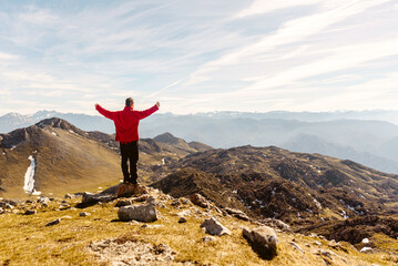 man on his back in red clothes and arms raised contemplating the mountain landscape after hiking up a mountain. sport, travel and adventure.