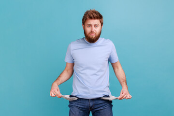 Man in blue T-shirt showing empty pockets and looking frustrated about loans and debts, has no money