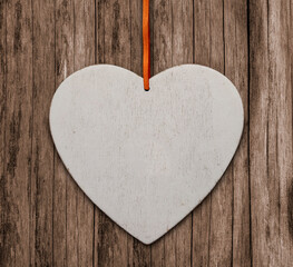 The image of the heart hangs on a ribbon on the background of a wooden surface