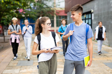 Two students holding bags and talking while walking