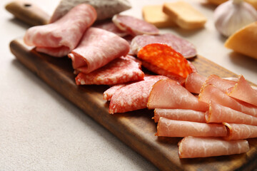 Wooden board with assortment of tasty deli meats on light background, closeup