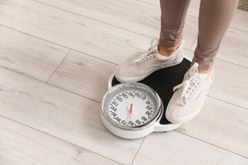 Sporty mature woman measuring her weight on scales at home, closeup