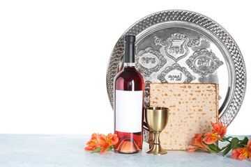 Passover Seder plate, bottle of wine, cup, flatbread matza and alstroemeria flowers on table against white background