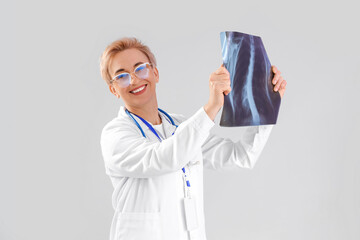 Mature female doctor with x-ray image of lungs on grey background