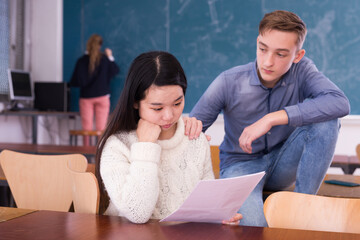 Girl and guy university students sitting at desk and preparing for exams together in classroom