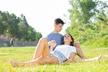 Couple of smiling teenagers sitting on green grass and points to something