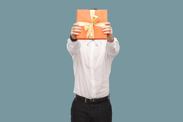 Unknown man holding out and covering his face with red gift box, giving present for anniversary.