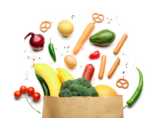 Paper bag with vegetables, sausage and fruits on white background