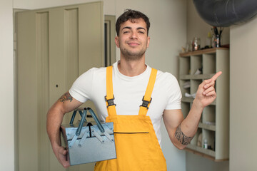 young handsome man smiling cheerfully, feeling happy and pointing to the side. handyman concept