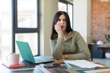 pretty young woman feeling scared, worried or angry and looking to the side. laptop and desk concept