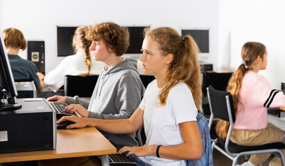 Pupils using computers at lesson, teacher teaching them in classroom