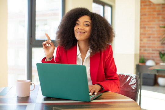 pretty afro black woman smiling cheerfully, feeling happy and pointing to the side. businesswoman and laptop concept