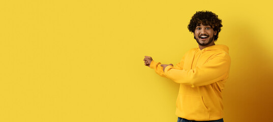 Positive indian guy in yellow hoodie pointing at copy space