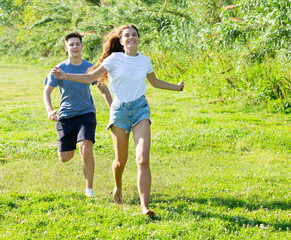 Two teenagers are running on the grass in summertime