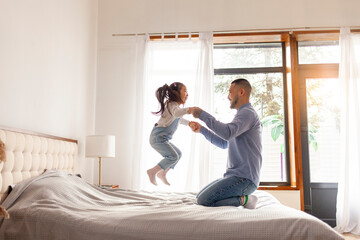 little asian girl jumping on bed at home with dad, korean man playing with daughter, happy family,...