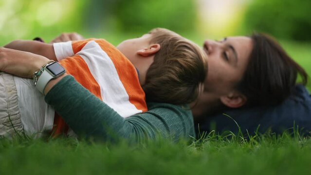 Mother laying down on grass with little boy son at park during beautiful sunny day. Parenting happiness concept