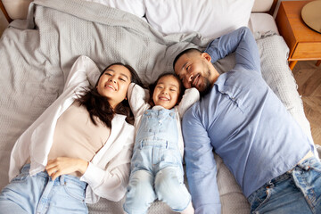 happy asian family lies together on the bed at home, little korean girl with mom and dad rest at...