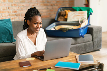 Positive black woman planning vacation travel with laptop, booking tickets or hotel room on web,...