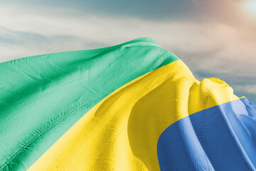Gabon national flag cloth fabric waving on beautiful grey sky.