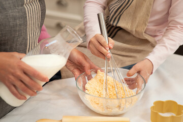 Hands of caucasian young mother and little daughter make cookie dough with whisk and milk