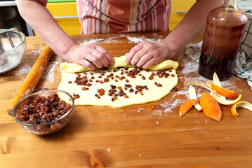 Woman baker rolls raisins into pastry for making buns.