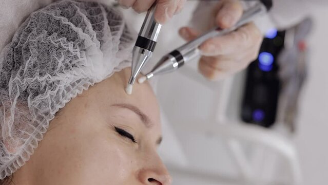 Electrical pulses for cosmetic procedures to smooth out wrinkles, restore, rejuvenate. Middle-aged woman receiving micro currents facial forehead skin treatment from beautician cosmetologist in clinic