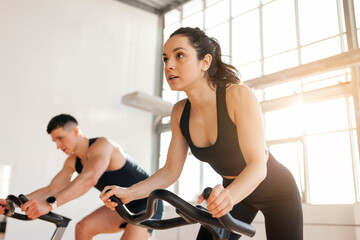 athletic couple of cyclists train on static bicycle simulator, man trainer and fitness woman go in...