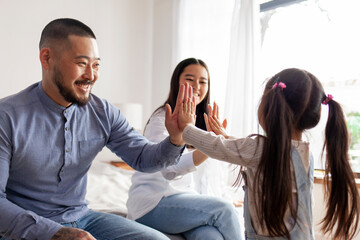 little asian girl play with mom and dad hands and palms, korean kid high five to dad and mom at home