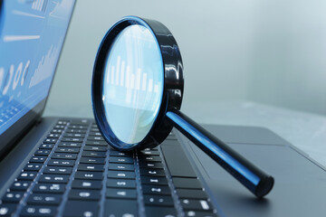 Magnifying glass on keyboard of laptop against light grey background, closeup