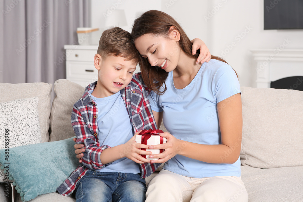 Poster Little boy presenting his mother with gift on sofa at home