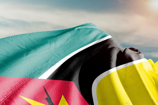 Mozambique national flag cloth fabric waving on beautiful grey sky.