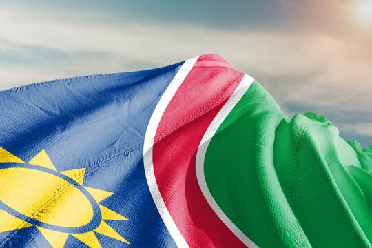 Namibia national flag cloth fabric waving on beautiful grey sky.