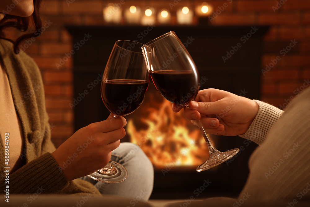 Poster Lovely couple with glasses of wine spending time together near fireplace at home, closeup