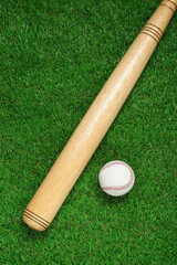 Wooden baseball bat and ball on green grass, flat lay. Sports equipment
