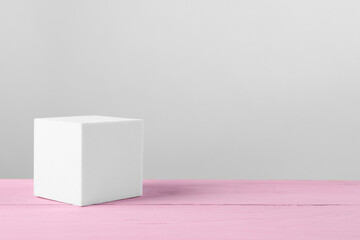 White cube podium on pink wooden table. Space for text