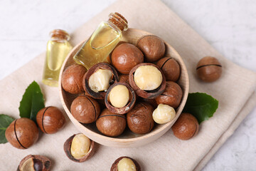 Bowl with organic Macadamia nuts and natural oil on white textured table, above view