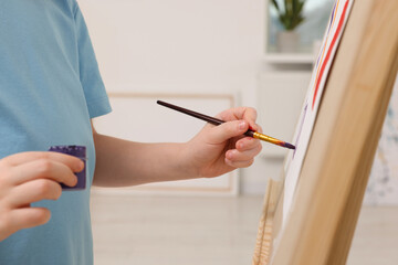 Little boy painting in studio, closeup. Using easel to hold canvas