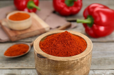 Bowl with aromatic paprika powder on wooden table, closeup