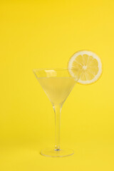 Martini glass of refreshing cocktail with lemon slice on yellow background