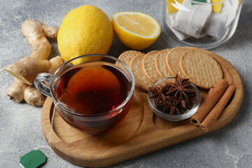 Tea bags, cup of hot drink, cookies and ingredients on light grey table